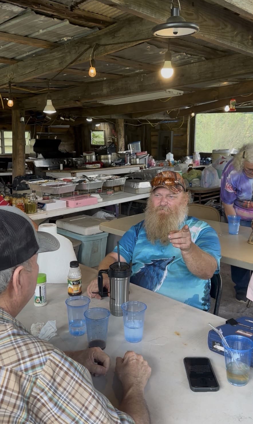 Tribal member with a big beard pointing and laughing at the table at Green Corn Ceremony 2026